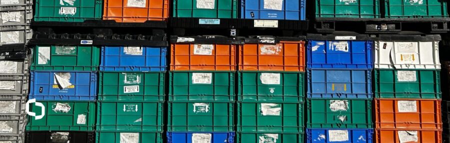 A stacked array of colorful industrial totes, including green, orange, and blue Handheld Totes (HHTs), used for organized storage and transportation in industrial settings. The image showcases the durability and versatility of these reusable containers for various applications.