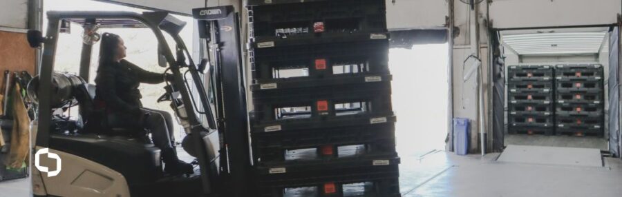 A forklift operator moves a stack of reusable containers into a loading dock, with additional containers visible in a trailer. The scene illustrates the efficiency of container leasing in supply chain operations, highlighting the practicality of leasing vs buying for scalable logistics.