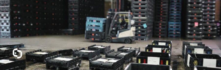 A warehouse scene focused on supply chain optimization, featuring black reusable containers scattered on the floor and stacked in the background. A forklift moves a load of containers, emphasizing efficient container services in a high-volume logistics environment. The organized storage system highlights streamlined inventory management and supply chain efficiency.