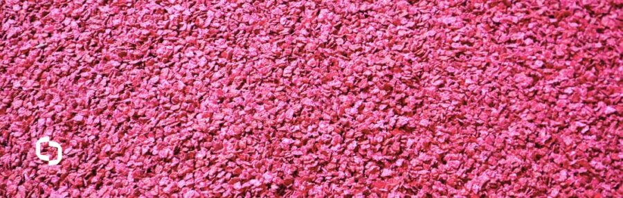 Close-up of vibrant red plastic regrind flakes, representing raw material used in plastic compounding and the refining regrind process to create high-quality recycled plastics.