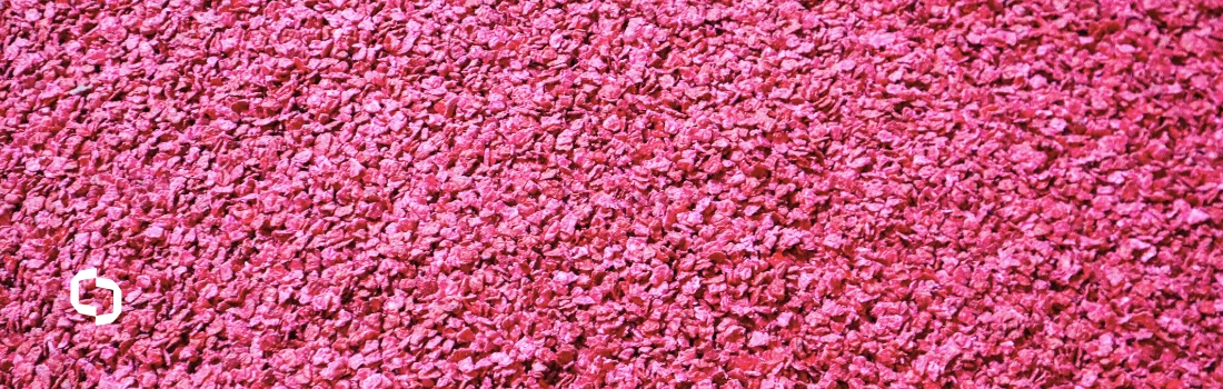 Close-up of vibrant red plastic regrind flakes, representing raw material used in plastic compounding and the refining regrind process to create high-quality recycled plastics.