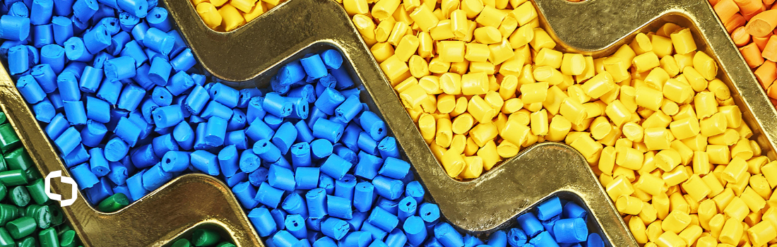 Colorful plastic pellets in shades of blue, yellow, green, and orange are separated by a metallic divider, representing plastic compounding and refining regrind. This image highlights the process of transforming raw plastic materials into high-quality, reusable compounds for manufacturing and sustainability.