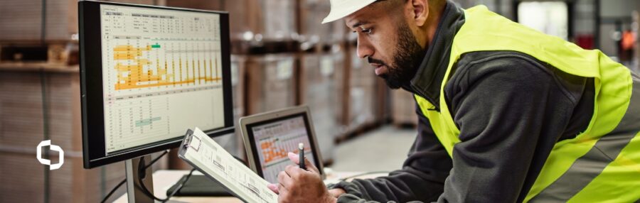 An Extera team member in a high-visibility vest and helmet analyzes logistics data on a computer in a warehouse, using AI-driven software to optimize inventory and supply chain processes. This image reflects Extera’s use of AI to enhance manufacturing efficiency.