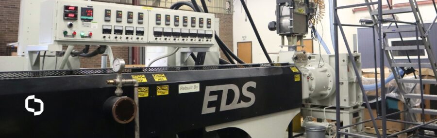 Industrial compounding process setup featuring plastic process equipment, including an EDS extruder machine with multiple control panels and tubing connections. This plastic processing equipment is used in manufacturing to blend raw plastic materials for reuse or product development.