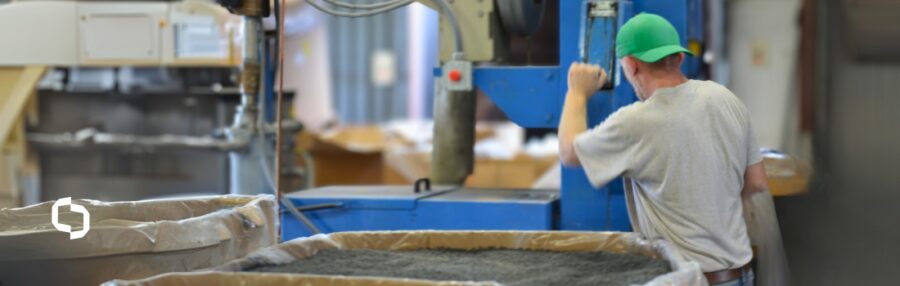 Worker operating plastic pelletizing equipment with bins of recycled plastic pellets in a production facility.