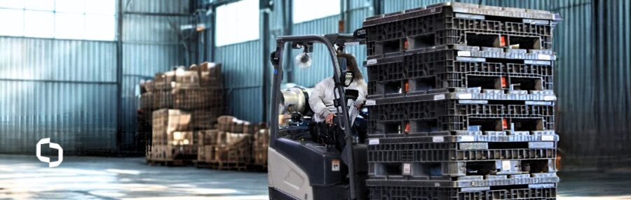 Worker driving a forklift inside a warehouse, moving stacks of reusable plastic bins, illustrating the leasing of containers as part of Extera’s container services.