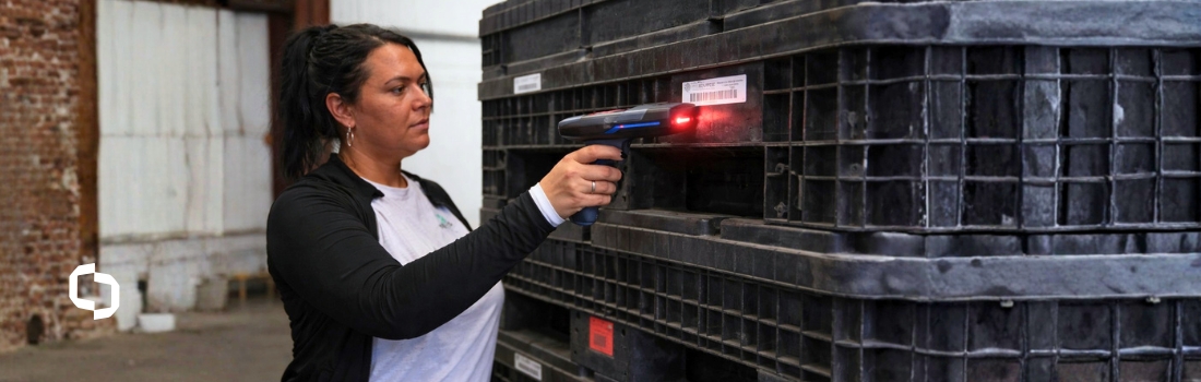 Warehouse worker scanning a barcode on stacked reusable containers for asset tracking in logistics management