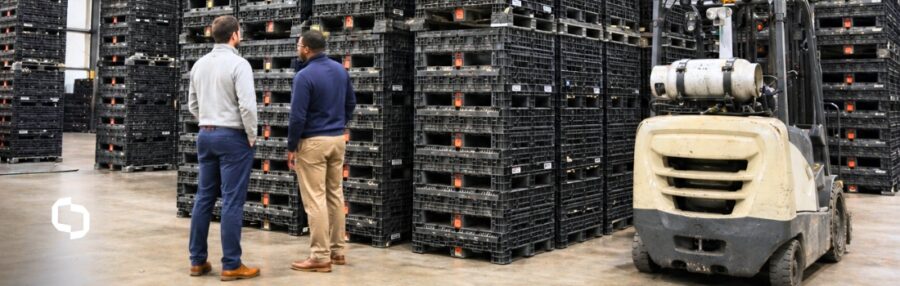 Warehouse team inspecting stacked reusable bulk containers before forklift transport.